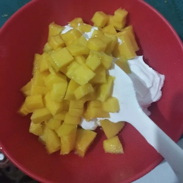 Mix bubuk whip cream dengan air es menggunakan mixer sampai kaku. Potong buah mangga kecil-kecil lalu campur keduanya, aduk rata.