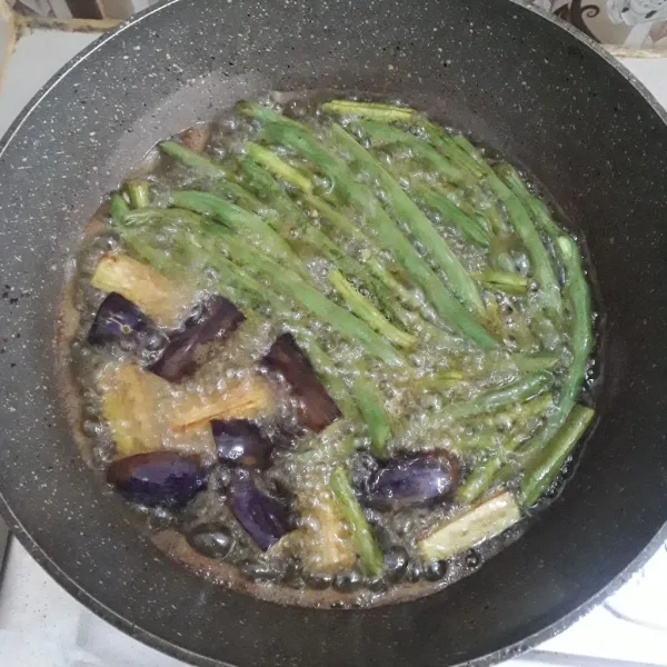 Panaskan minyak goreng. Masukkan buncis, kacang panjang dan terong. Goreng sampai sayuran matang/empuk.