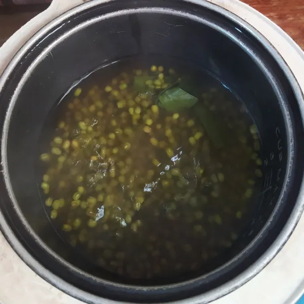 Masukkan kacang hijau, daun pandan dan air ke dalam panci magic com, lalu tekan tombol on. Kalau sudah mendidih selama 5 menit, cabut  kabel magic com dari stop kontak. Lalu diamkan selama 30 menit dalam keadaan tertutup.