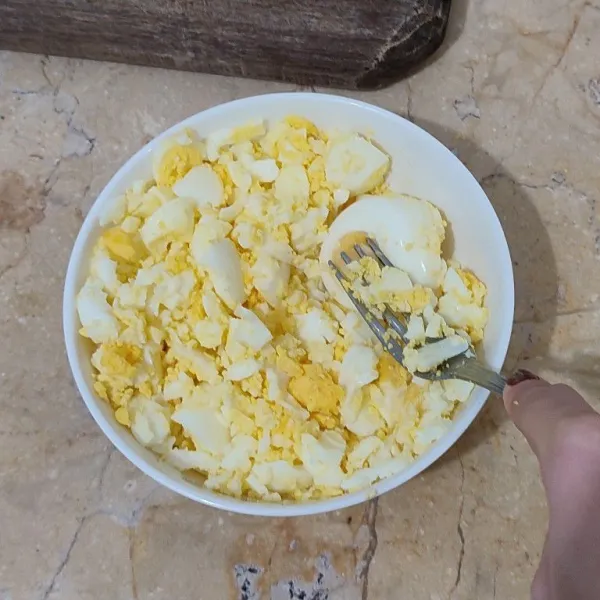 Kupas telur rebus dan hancurkan telur rebus dengan garpu.