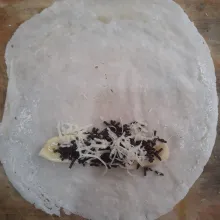 Letakkan potongan pisang di atas kulit lumpia. Tambahkan meises dan parutan keju di atas pisang.