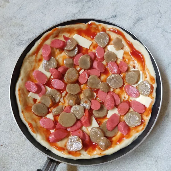 Olesi pizza dengan campuran bahan saus hingga rata. Beri sobekan satu lembar keju lumer lalu tata tumisan baso dan sosis.