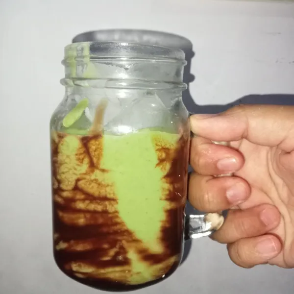 Tuang kental manis coklat ke dalam pinggiran gelas lalu tuang alpukat ke dalam gelas. Tambahkan es batu (jika suka) dan sajikan.