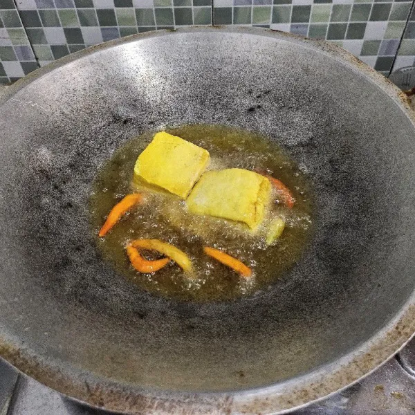 Goreng tahu dalam minyak panas. Jika tahu sudah hampir matang masukkan cabe dan bawang putih. Goreng sebentar lalu tiriskan.
