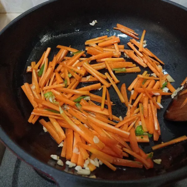 Panaskan minyak goreng, tumis bawang putih cincang sampai harum dan mulai kecoklatan, masukkan wortel, aduk rata.