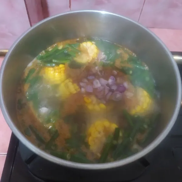 Tuang bumbu sayur asem instan dan beri irisan bawang merah.