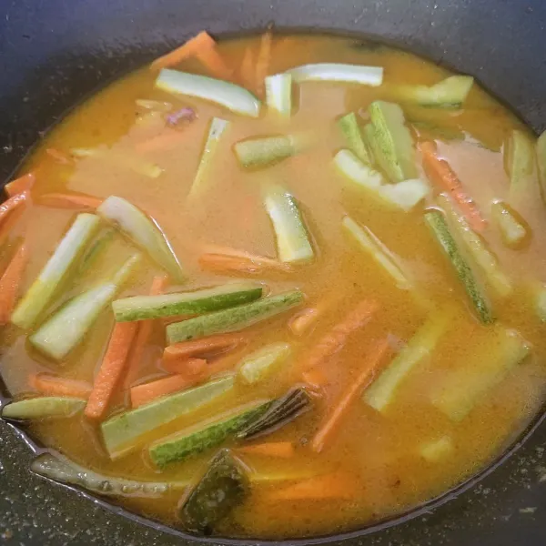 Tambahkan air, kemudian masukkan timun dan wortel yang sudah dipotong memanjang, masak hingga mendidih dan air sedikit surut.