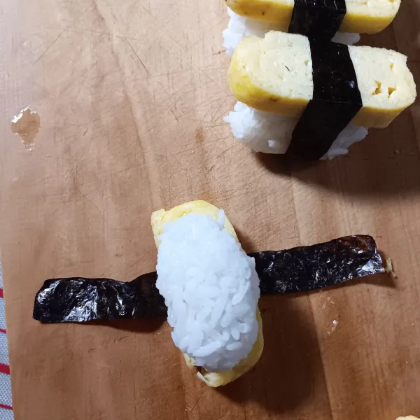 Bentangkan nori. Letakkan potongan telur ditengah, timpa dengan nasi kepal. Arahkan nori ketengah hingga mengikat nasi dan telur. Lakukan sampai selesai.