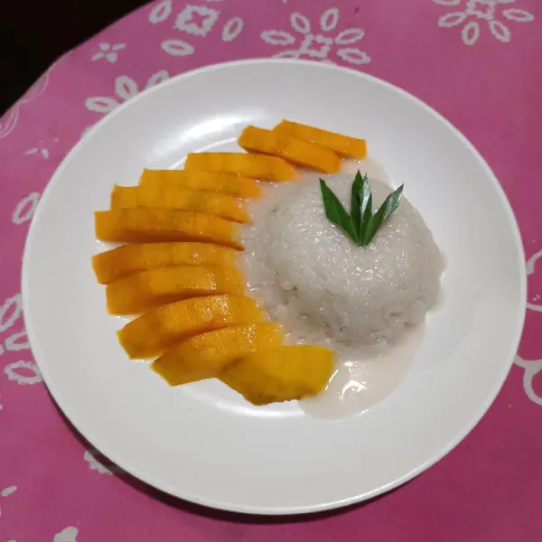 Sajikan mango sticky rice dengan meletakkan ketan dengan potongan mangga lalu siram dengan fla santan.