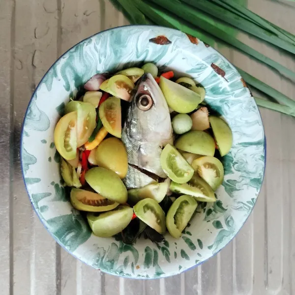 Siapkan wadah, tata daun salam, ikan, cabai, tomat, kencur, dan lengkuas