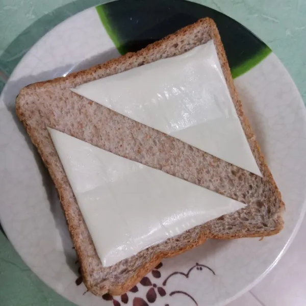 Beri keju slice yang dipotong segitiga di atas roti tawar gandum.