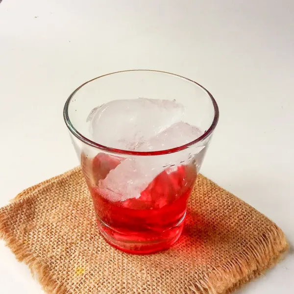 Tuang sirup merah di gelas, beri es batu.