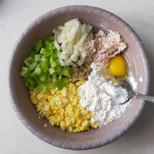 Siapkan wadah, kemudian masukkan jagung yang sudah di ulek tadi. Beri bumbu halus, tepung terigu, tepung maizena, daun bawang, bawang bombai, udang rebon, dan telur.