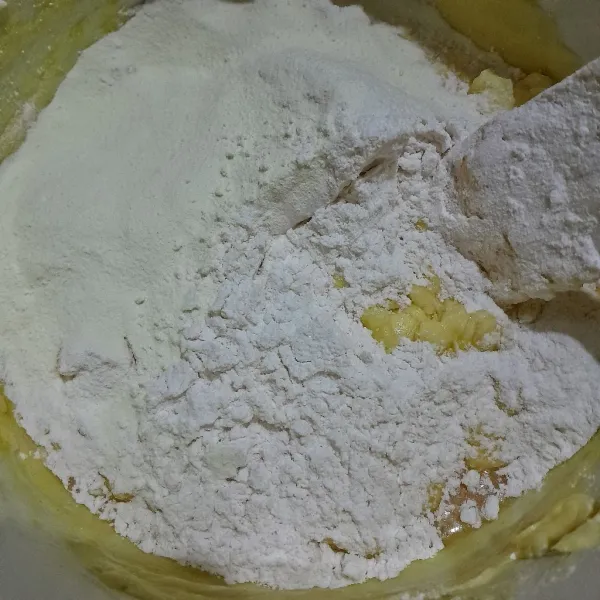 Sebelumnya, ayak tepung terigu, tepung custard, baking powder, vanili bubuk, dan susu bubuk. Masukkan ayakan tepung secara bertahap ke adonan lalu aduk hingga tercampur dengan baik.