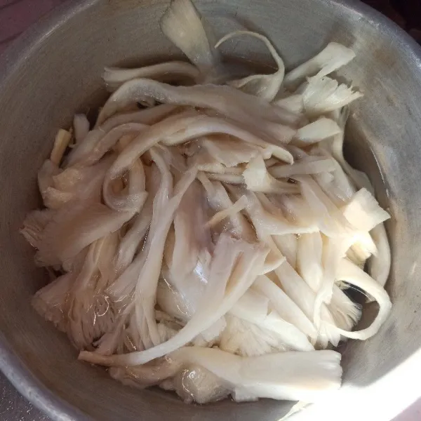 Suwir-suwir jamur tiram kemudian rendam dengan air panas, diamkan beberapa saat kemudian bilas sampai bersih, lalu peras.