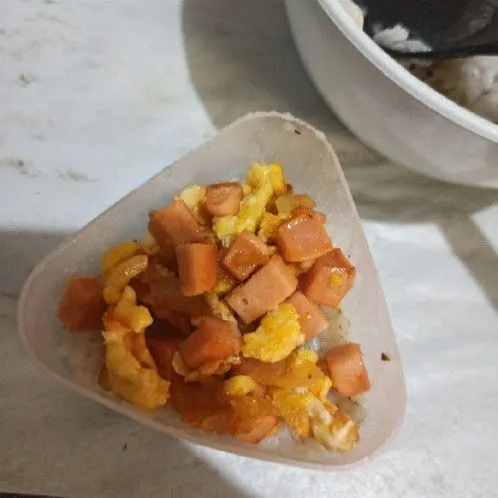 Ambil cetakan onigiri, beri nasi bagian bawah, bagian tengah sosis telur
