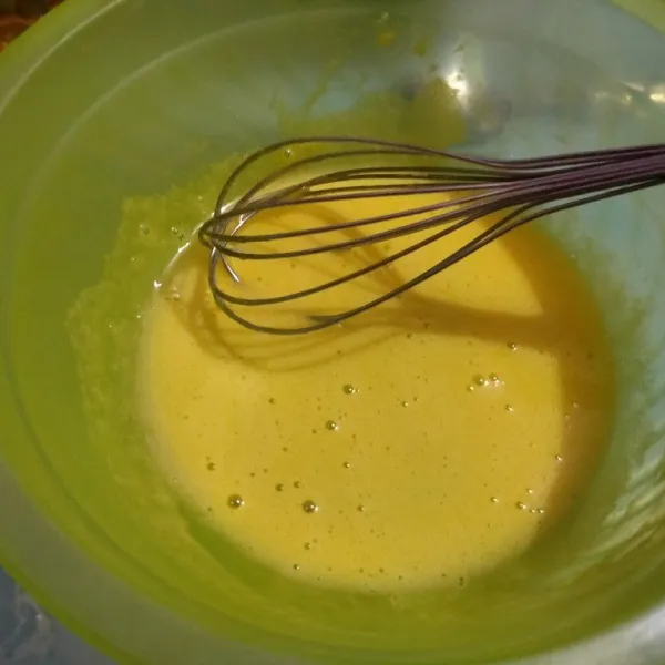 Di wadah lain, kocok kuning telur dan gula pasir menggunakan whisk sampai pucat dan agak mengental
