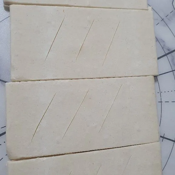 Siap puff pastry lalu potong dengan ukuran 4 cm× 10 cm sebanyak 16 lembar. Yang 8 lembar kita sayat 3x bagian atasnya, sedangkan yang 8 lembar lagi tidak disayat.