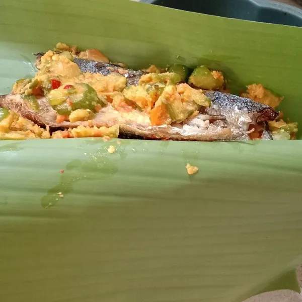 Bungkus ikan pindang yang telah dilumuri bumbu dengan daun pisang.