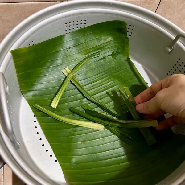 Taruh lembaran daun pisang di kukusan dan tata daun pandan.