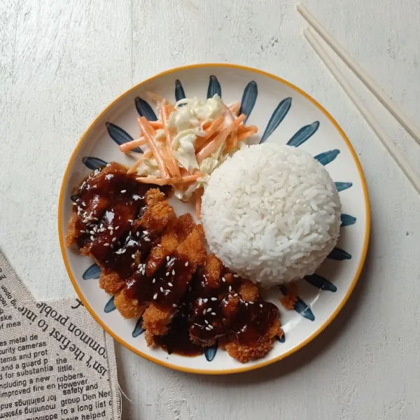 Potong-potong Katsu lalu tata pada piring siram dengan saus lada hitam, sajikan dengan nasi hangat dan salad kol wortel.