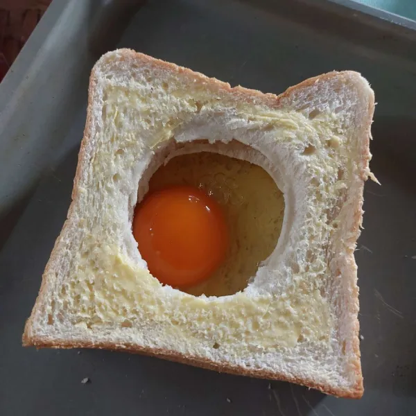 Susun ketiga roti tawar dengan yang bolong di atas, lalu pecahkan telur, masukkan ke dalamnya.