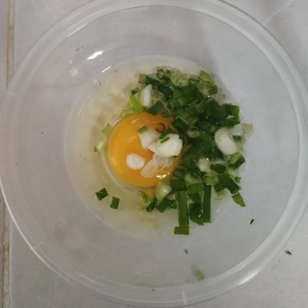 Pecahkan telur dalam wadah, lalu beri  irisan daun bawang dan seledri
