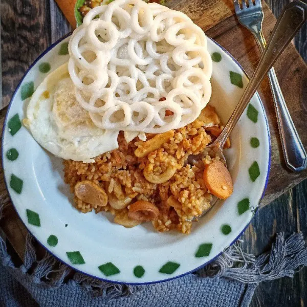 Sajikan nasi goreng tom yum dengan telur ceplok dan kerupuk.