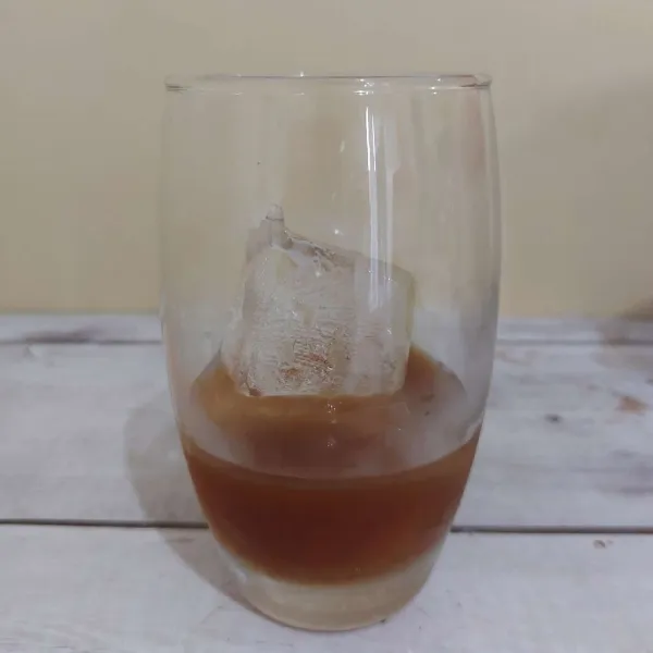 Tuang sirup gula merah ke gelas berisi es batu.