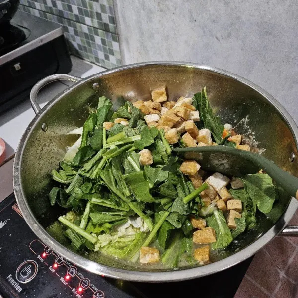 Jika sawi putih sudah setengah matang, masukkan caisim dan tahu goreng.