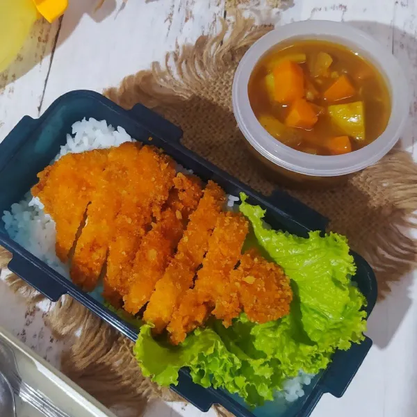 Tata nasi di kotak bekal, beri daun selada dan chicken katsu. Letakkan kare di wadah lain. Siap untuk dibawa ke sekolah ataupun kantor.