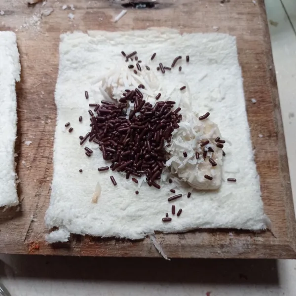 Ambil selembar roti tawar, beri isian pisang iris, keju parut dan mesis coklat.