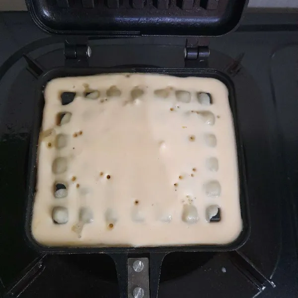 Oles cetakan waffle dengan mentega lalu panaskan, setelah itu tuang adonan waffle dan masak hingga matang.