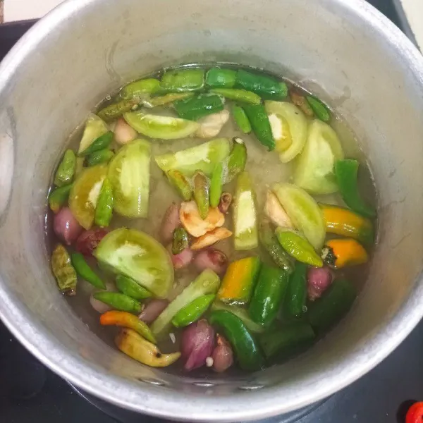 Didihkan air kemudian rebus cabe hijau, rawit hijau, tomat hijau, bawang merah, bawang putih dan kemiri sampai empuk.