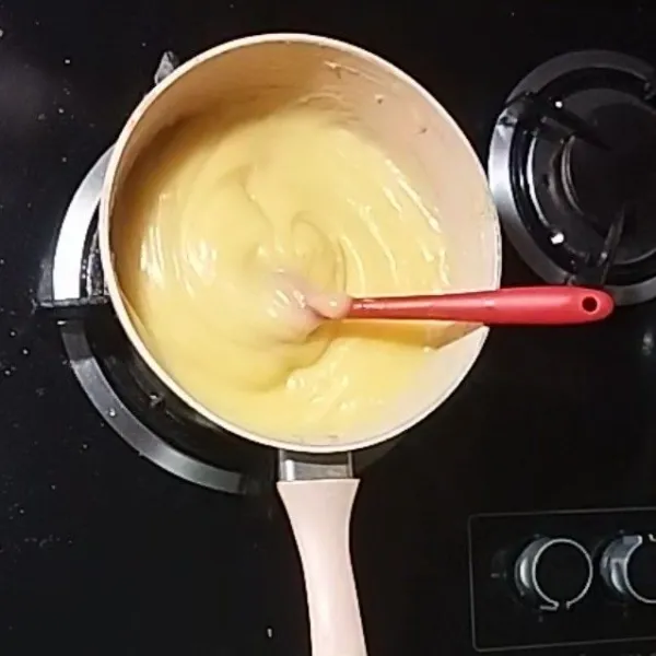 Setelah uap hilang, tuang perlahan-lahan adonan kuning telur ke dalam panci sambil diaduk rata. Kemudian panaskan kembali sampai custard mulai solid sambil terus diaduk. Matikan kompor, masukkan mentega dan pasta vanila aduk hingga tercampur rata. Dinginkan.