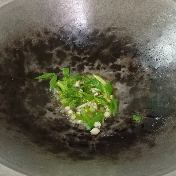 Tumis bawang putih geprek dan irisan daun bawang hingga harum.