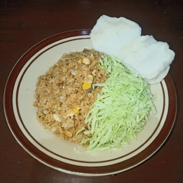 Sajikan nasi goreng dengan pelengkap berupa kol yang diiris tipis dan kerupuk.