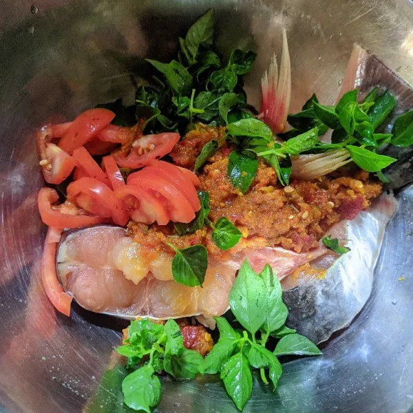 Masukkan bumbu halus, daun kemangi, tomat yang sudah dipotong potong ke dalam mangkuk berisi ikan.