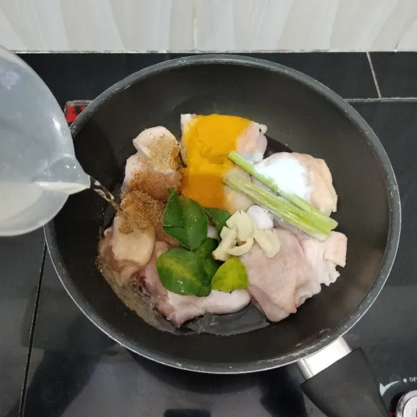 Masukkan ayam ke dalam panci. Tambahkan serai, kunyit bubuk, ketumbar bubuk, bawang putih, daun jeruk, dan garam. Lalu tambahkan air dan aduk rata.