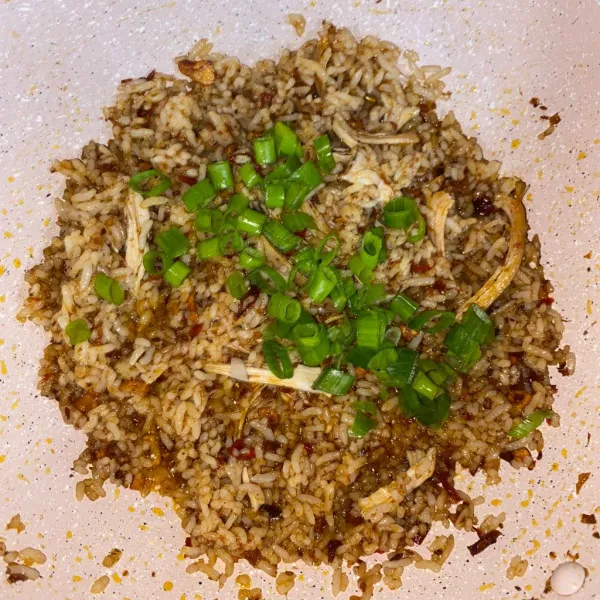 Tambahkan daun bawang, aduk sebentar sampai layu. Angkat nasi goreng lalu sajikan dengan bahan pelengkap.