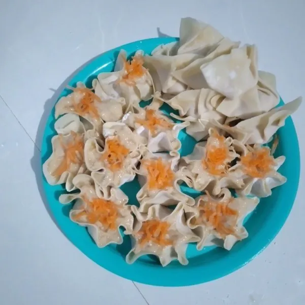 Ambil kulit dimsum, masukkan adonan dan bentuk sesuai selera. Tambahkan parutan wortel di atasnya.