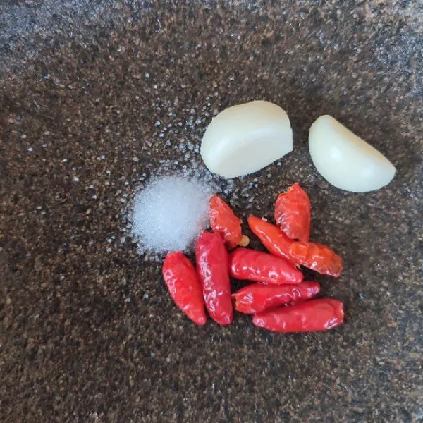 Kupas cabe rawit dan bawang putih lalu letakkan bersama garam di atas cobek.