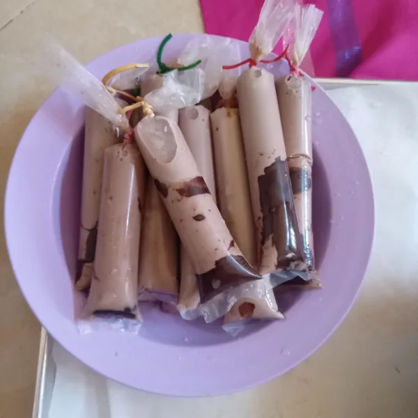 Tuang cairan susu ke dalam plastik es yang berisi dark cooking chocolate leleh tadi, masukkan sebanyak 1/3 bagian lalu ikat plastik, lalu rendam ke dalam baskom yang berisi air dingin, lakukan sampai semuanya habis.