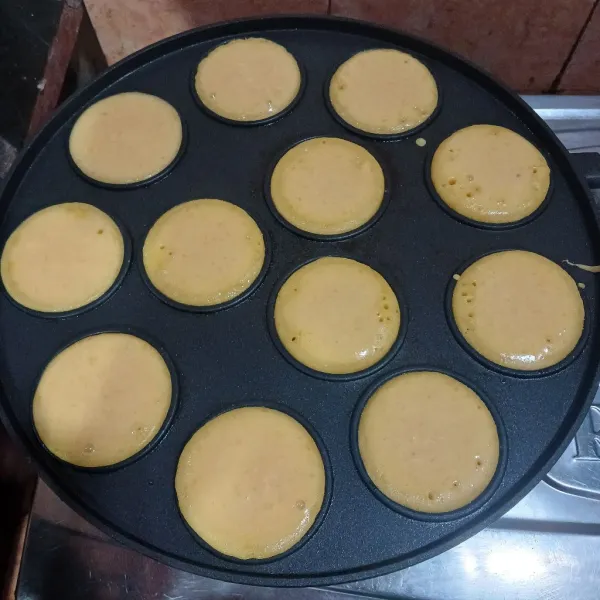 Panaskan cetakan kue lumpur, lalu tuang adonan hingga penuh. Jika bagian atas mulai mengeras, beri toping choco chips atau kismis. Tutup dan panggang hingga matang.