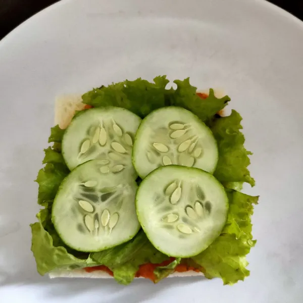 Letakkan 1 lembar daun selada dan irisan timun di atas roti