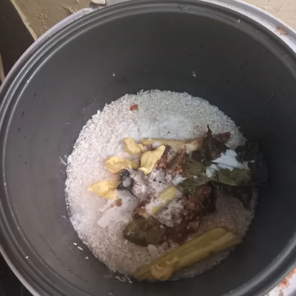 Cuci beras dan beras ketan lalu campurkan saja dalam rice cooker masukan air dengan rasio 1:1. Tuangkan bumbu tumis, margarin dan santan. Bumbu jangan diaduk ke nasi biarkan saja menumpuk diatas nasi. Kalau diaduk nasinya malah tidak masak.