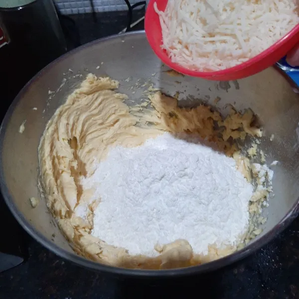 Masukan tepung, susu bubuk, dan keju parut aduk rata dengan spatula hingga tercampur dan uleni dengan tangan hingga kalis/tidak lengket di tangan, tutup adonan dengan plastik agar adonan tidak kering.