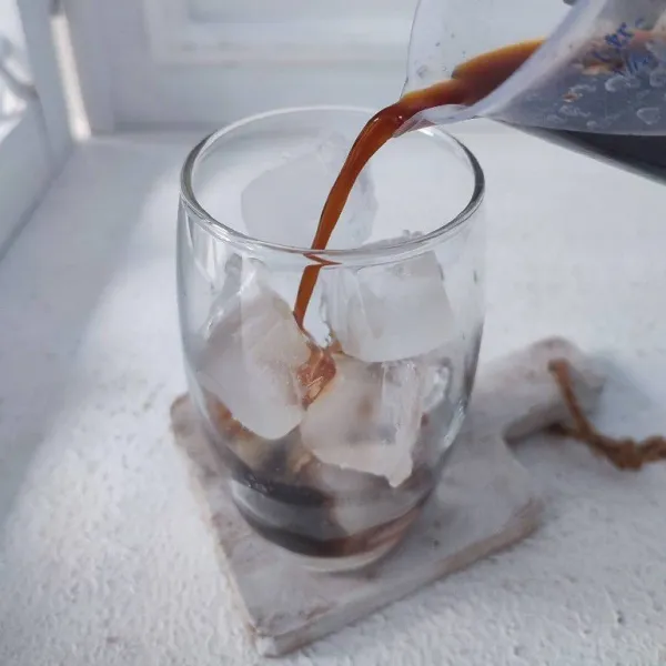 Siapkan gelas berisi es batu, tuang larutan kopi.
