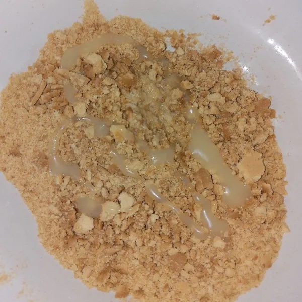 Tuang 1 sdt mentega cair dan 2 sdt susu kental manis ke dalam biskuit yang sudah dihaluskan.