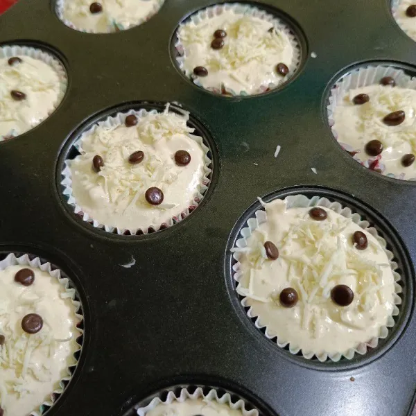 Siapkan cetakan muffin, beri kertas cupcake, tuang adonan dan beri topping keju parut dan choco chips
